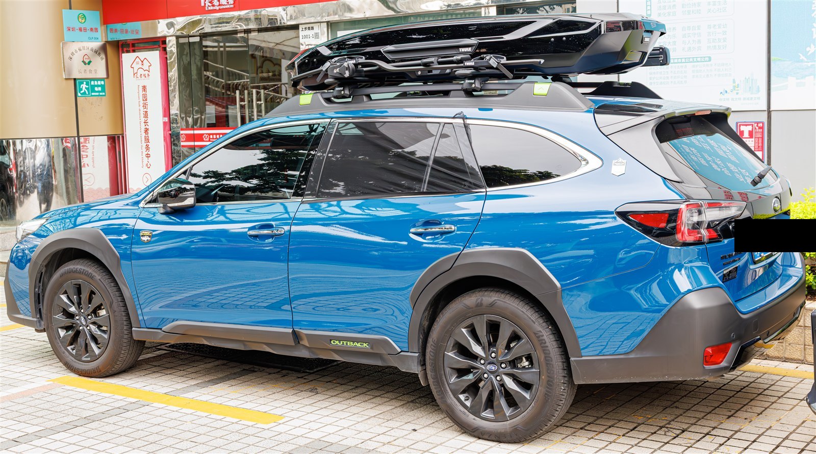 Subaru Outback with a Thule roof cargo box mounted, parked on a city street