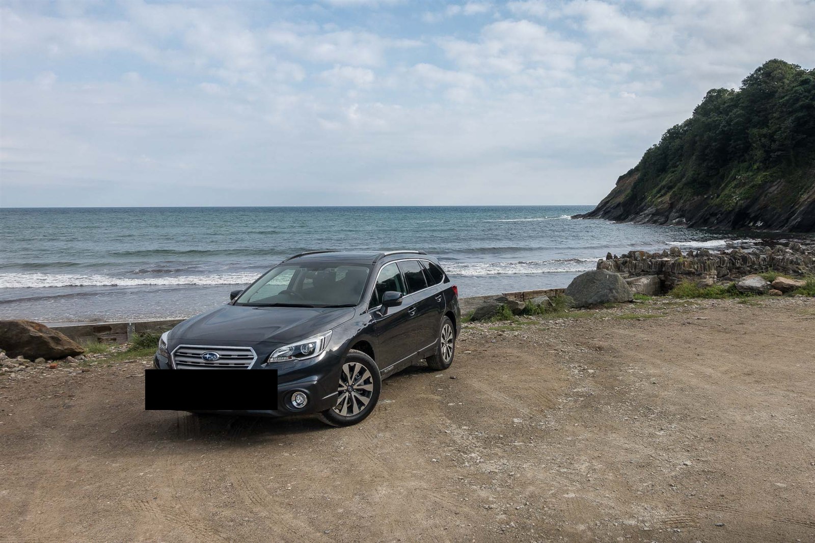 Subaru Outback parked on a gravel area overlooking a beach and cliffs