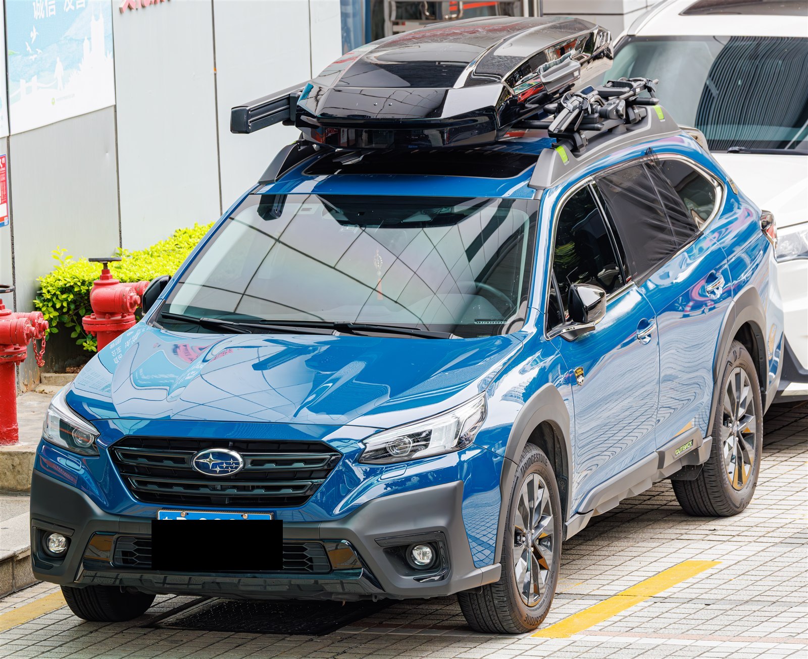 Blue Subaru Outback with a roof cargo box, front three-quarter view
