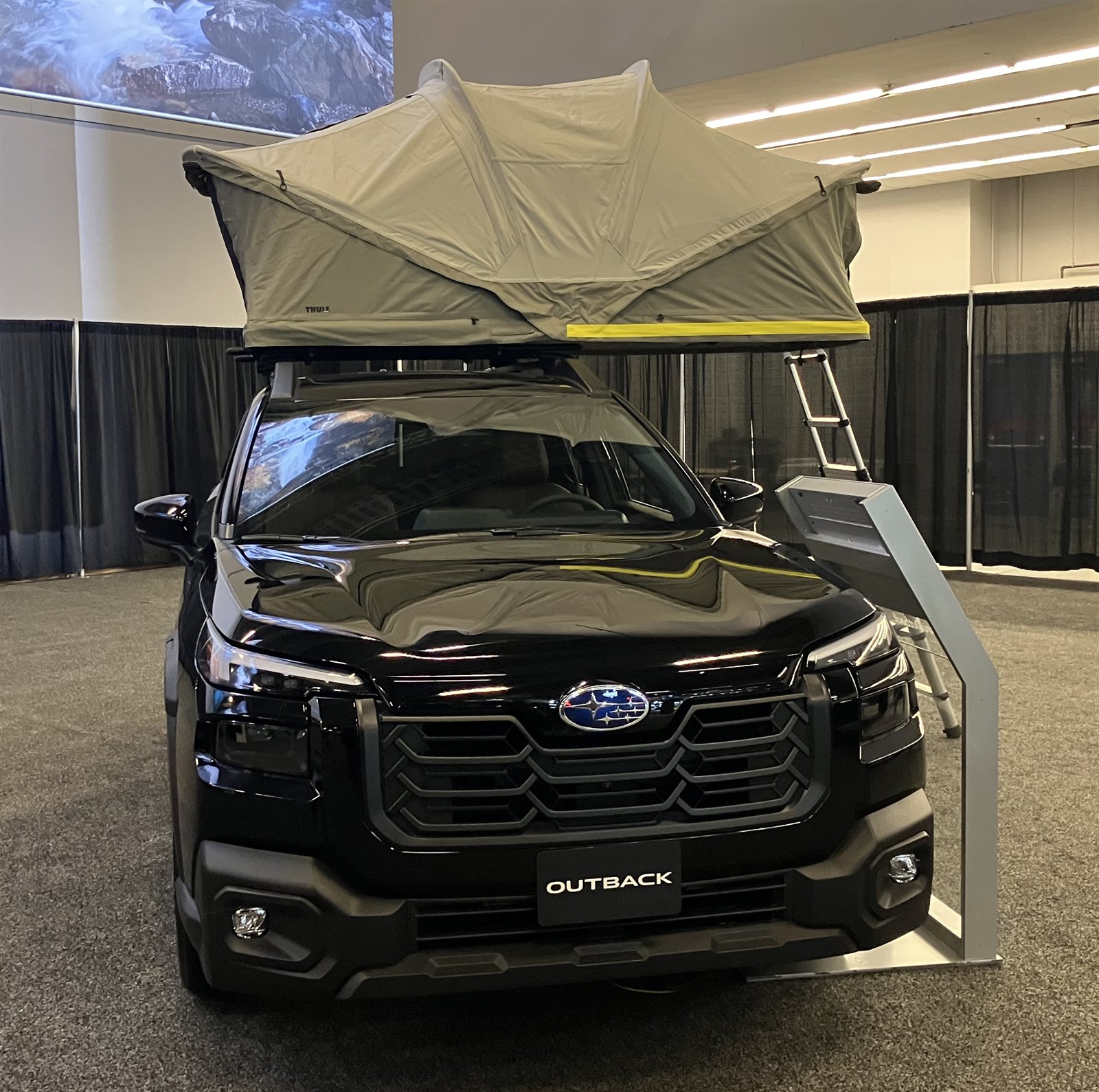 Black Subaru Outback with a Thule roof tent fully deployed, ladder extended