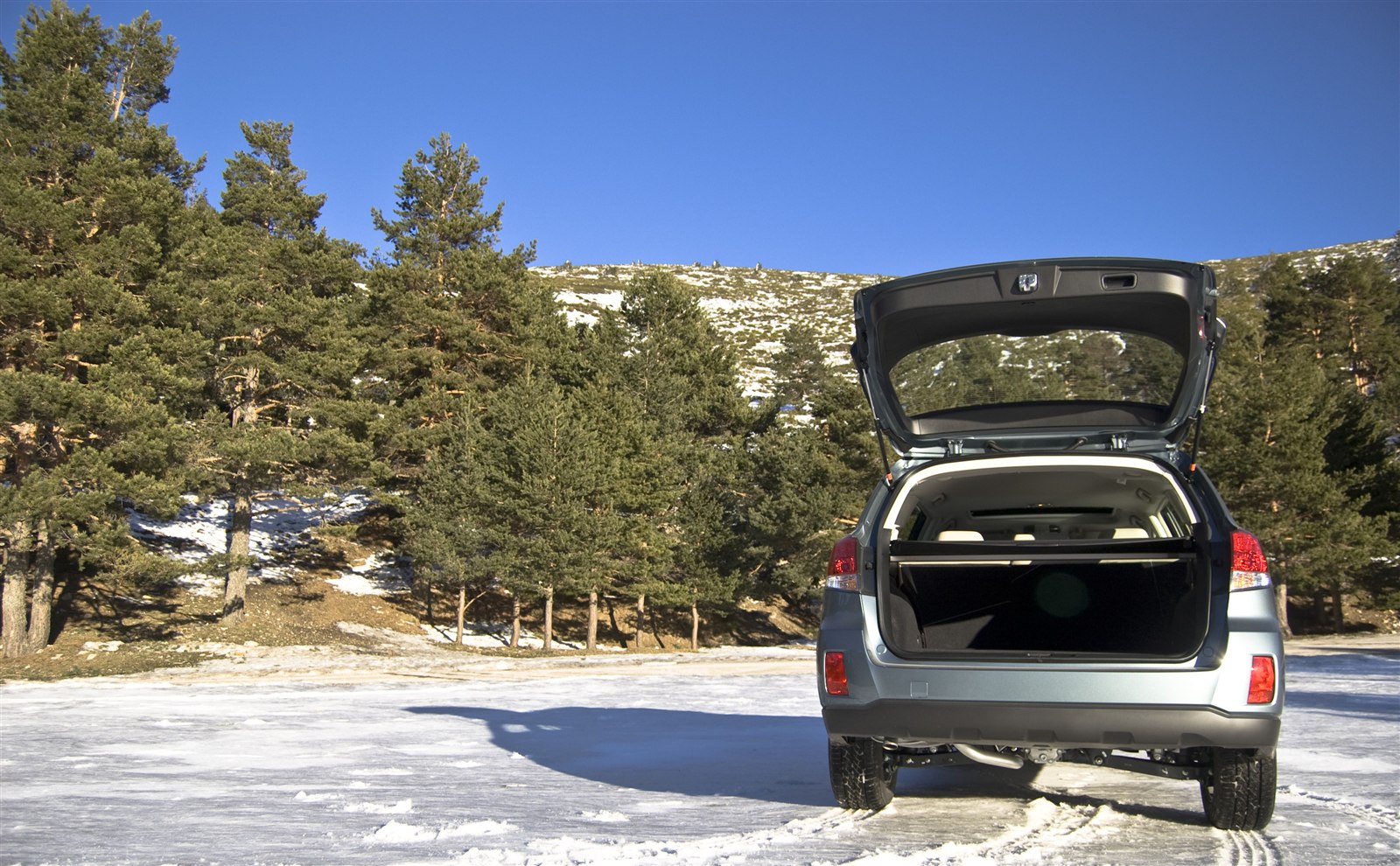 Subaru Outback with rear hatch open, parked in a snowy mountain setting